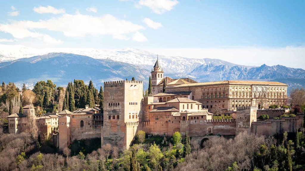 The Alhambra palace complex, one of the best places to visit in Spain, with the snow-capped Sierra Nevada mountains in the background, under a clear blue sky.