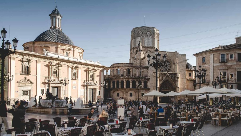 Historic European city square with outdoor dining, classic architecture, and winter sun in Spain.
