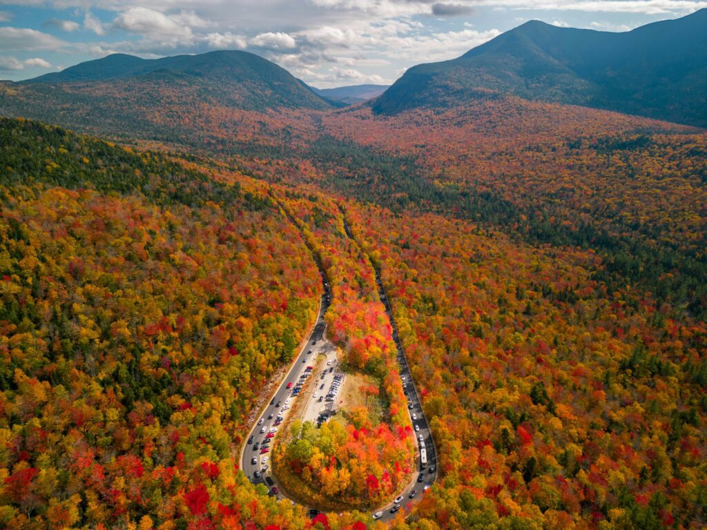 A horseshoe roadway embraced by fiery gold, orange, and red leaves in upstate New Hampshire.