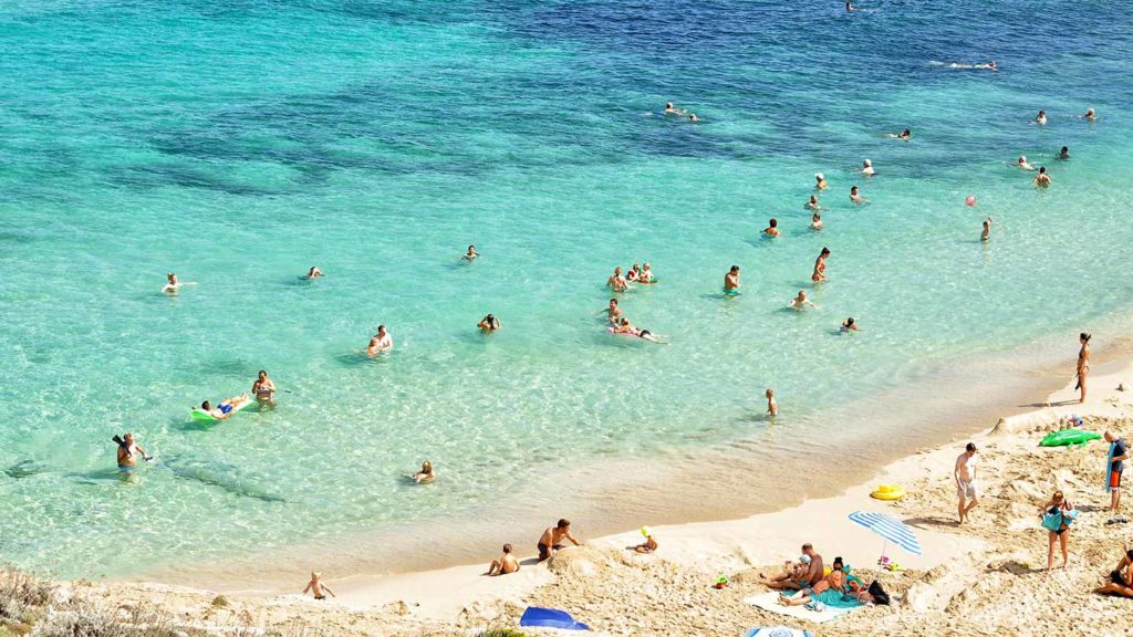 Beachgoers enjoying clear turquoise waters on a sunny day.