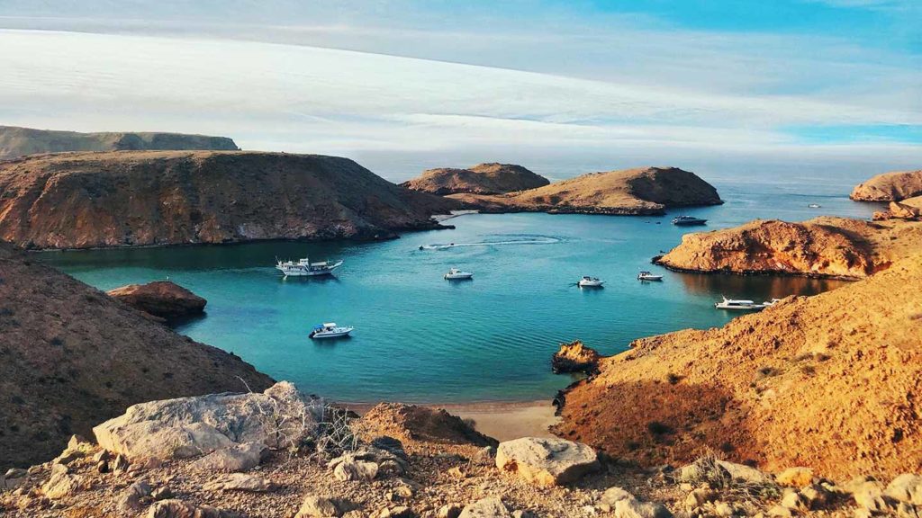 Boats anchored in a tranquil bay surrounded by arid hills under a clear blue sky, reminiscent of the world's friendliest countries.