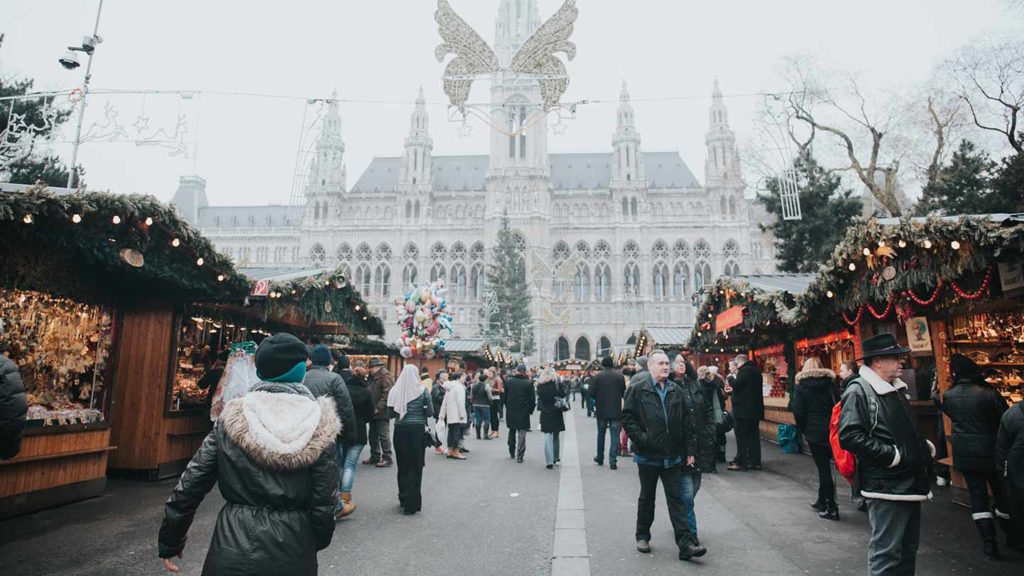 Holiday market in front of a historical building with festive decorations and visitors, rated as one of the best Christmas markets for those wondering where to travel for Christmas.
