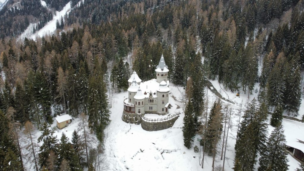 Aerial view of the House of Gucci castle nestled among snowy pine trees.