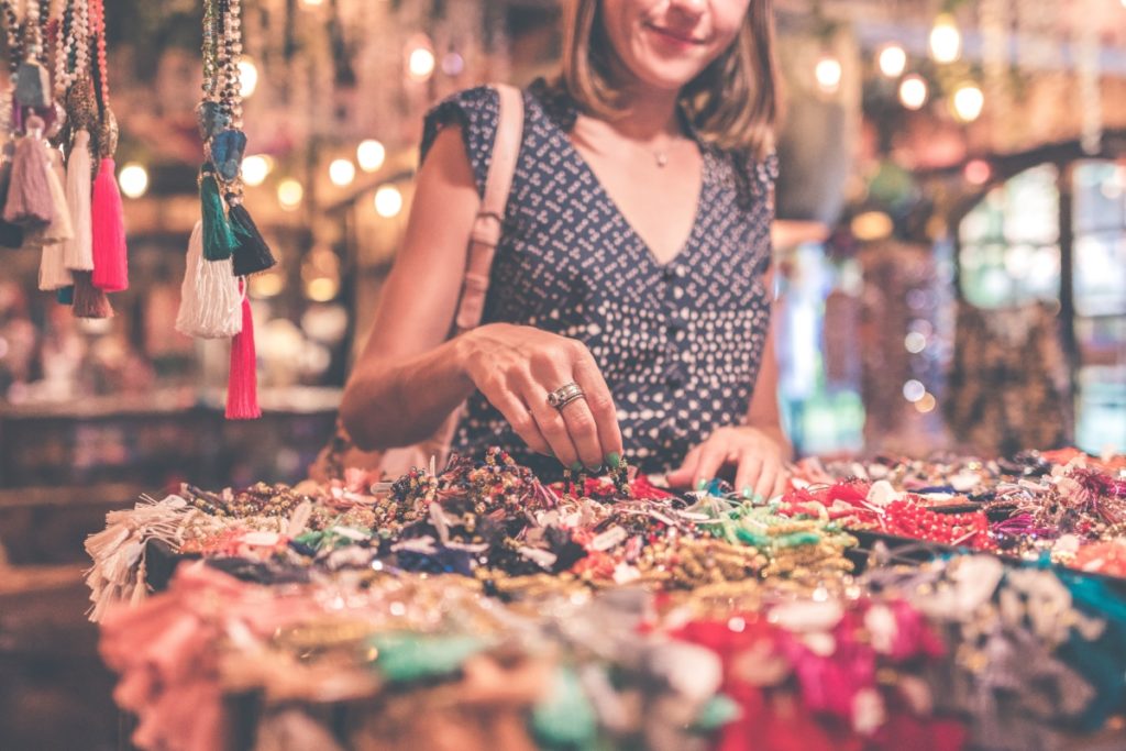 A woman browsing through a selection of colorful jewelry at a market stall practices responsible travel by supporting local artisans.
