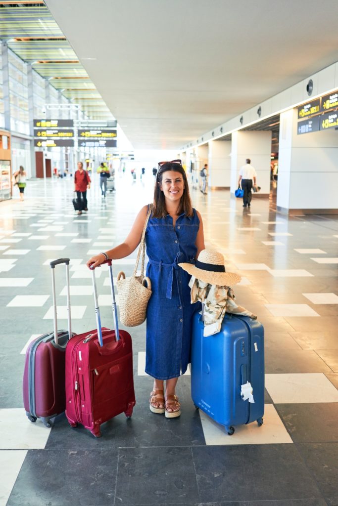 Woman standing in airport terminal with two suitcases, embodying the essence of travel alone for mental wellbeing.