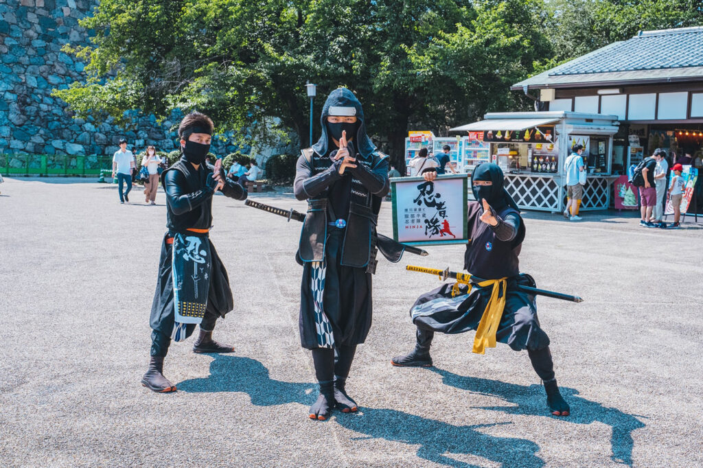 Three individuals dressed as ninjas posing for a photo at a cultural event, observing Japanese cultural etiquette.