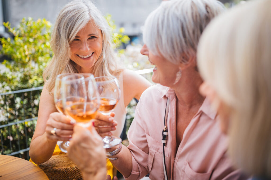 Three senior women smiling and toasting with wine glasses at an outdoor table in a travel magazine.