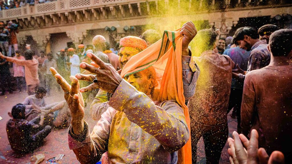 A man joyfully throwing yellow powder during Holi festival celebrations in India, surrounded by others in a vibrant, sunlit setting at one of the bucket list events.