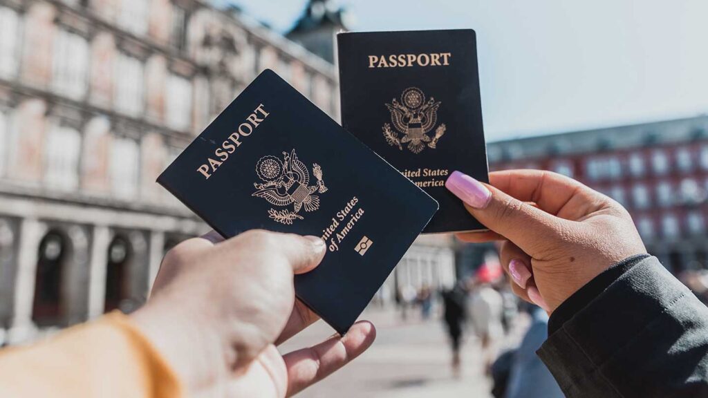 Two hands holding U.S. passports against an urban background, ready for hilarious travel stories.
