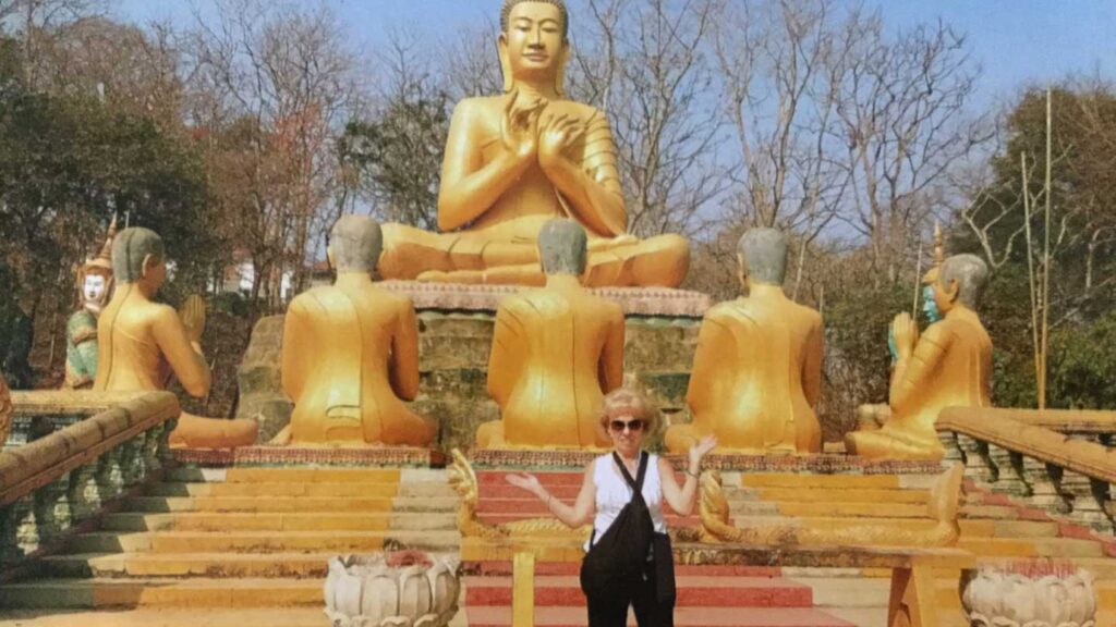 A woman, possibly a Trafalgar guest, stands in front of large golden Buddha statues arranged in a semicircle on a sunny day.