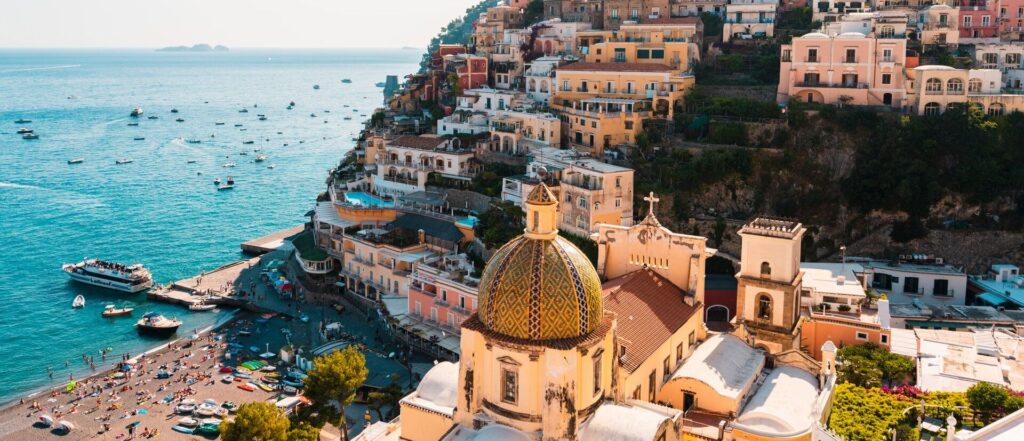Aerial view of Positano's colorful cliffside houses overlooking the beach and boats in the Mediterranean Sea, perfect for a travel magazine feature.