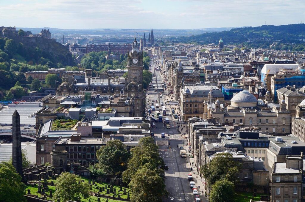 Aerial view of Edinburgh city center showing historic buildings along the main street, ideal for an affordable family vacation, with a backdrop of hills and clear skies.