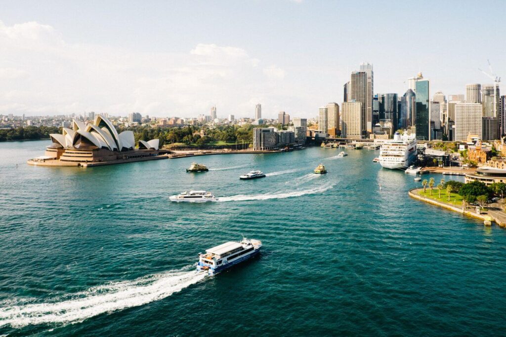 Aerial view of Sydney Harbour with the opera house, boats on water, and city skyline on a sunny day in September.
