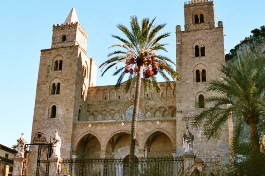 Front view of the cathedral in Cefalu, with a palm tree in front and palm tree to the right hand side.