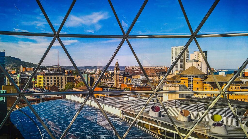 View of a cityscape through a geometric glass dome, featuring modern and historical buildings under a clear blue sky during a Trafalgar tour.