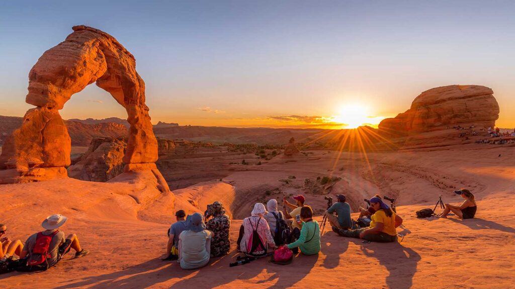 Family vacation: Group of people sitting and watching the sunset at Delicate Arch, Arches National Park, Utah.