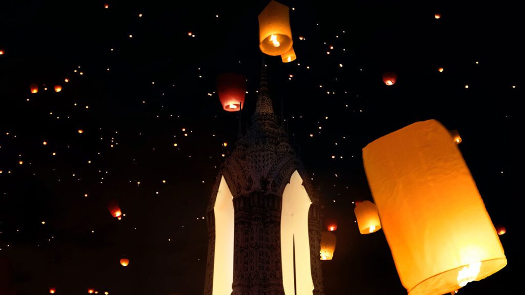 Floating lanterns ascend into the night sky near a traditional temple, inspiring kids to travel as they create a luminous spectacle against a dark background.
