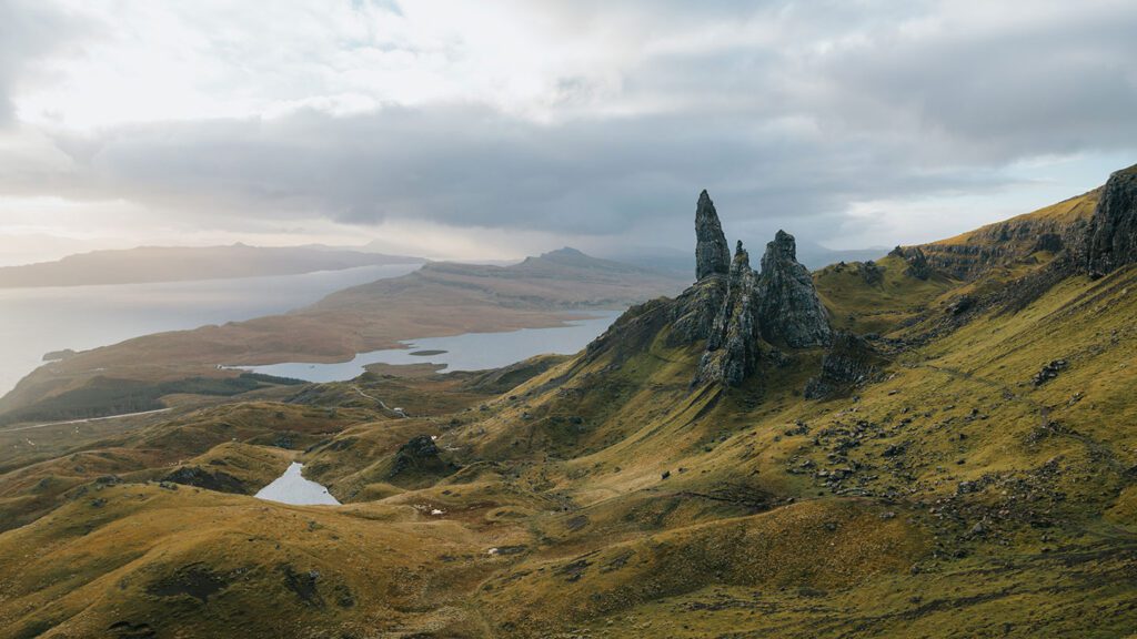 Panoramic view of the old man of storr rock formations with rolling hills and a distant lake in cloudy light, featured in our 2023 tours.
