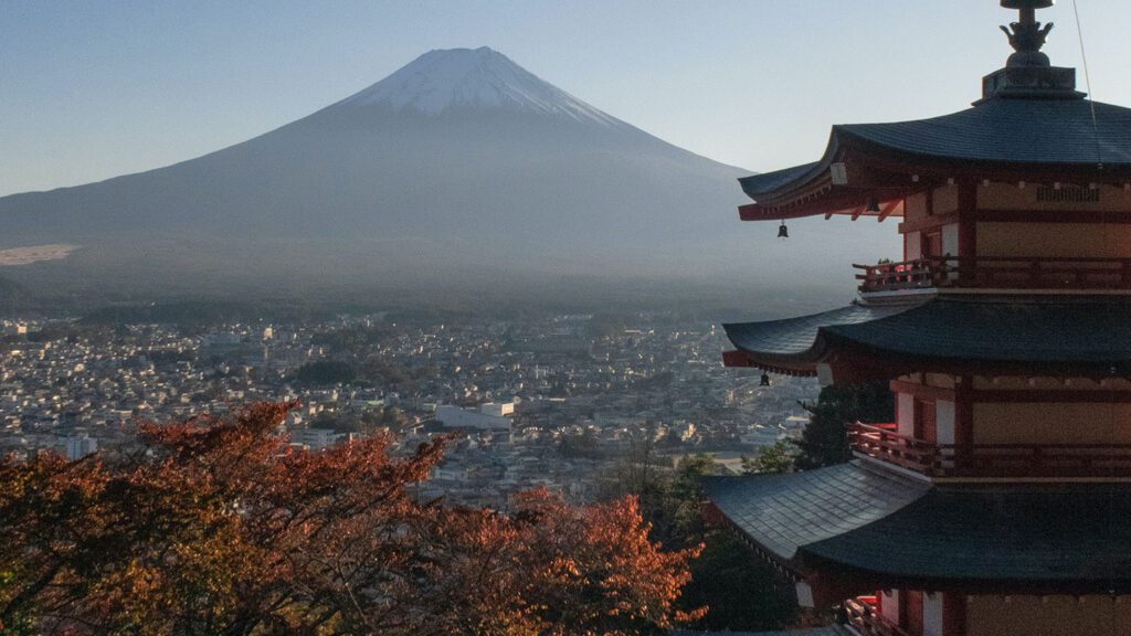 A view of Mount Fuji in the background with a multi-tiered pagoda on the right and the surrounding town visible in the fading light, capturing one of the essential things to do in Japan.