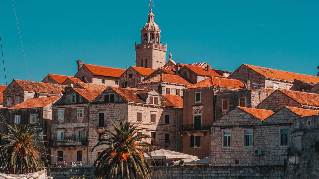 Historic Balkan town with orange tiled roofs and a prominent stone bell tower under a clear blue sky.