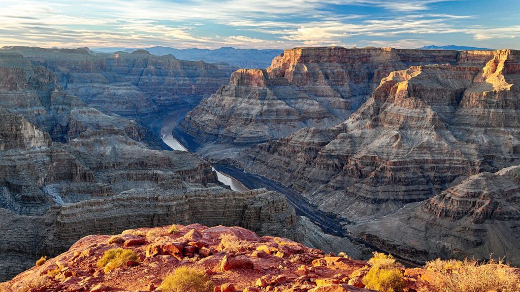 A panoramic view of the grand canyon with the Colorado River winding through it, taken at sunrise, showcasing one of the top destinations for travelers worldwide.