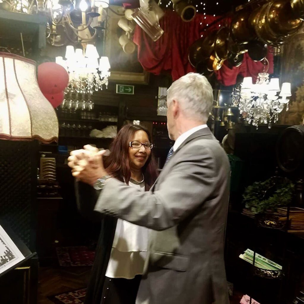 A man and a woman dancing together in a room filled with antique decor and warm lighting.