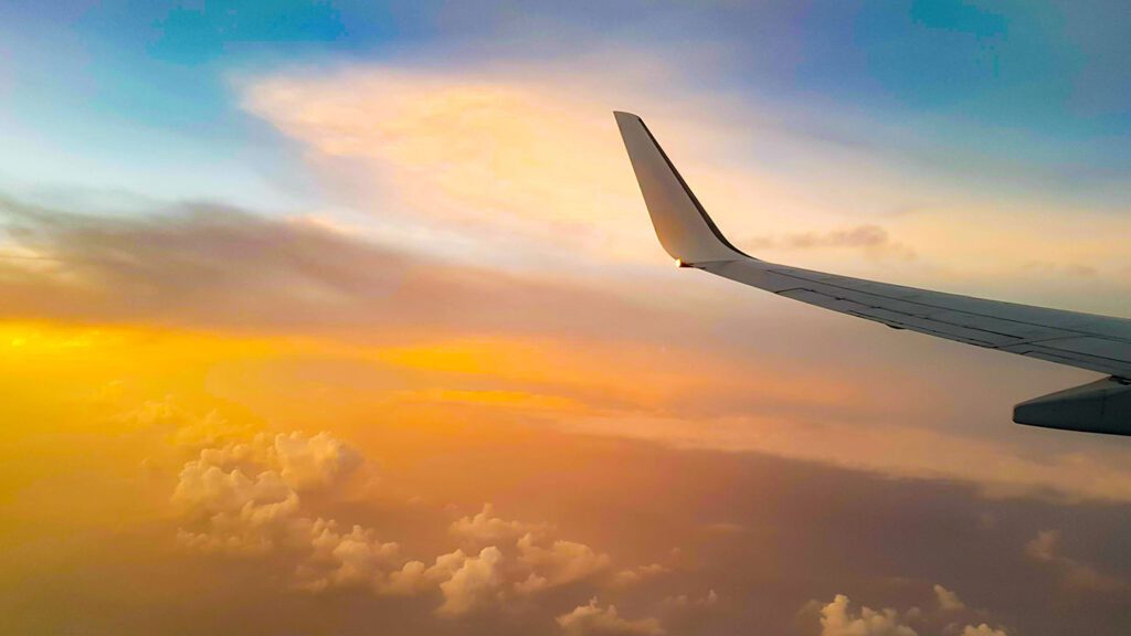 View from an airplane window showing the wing with a backdrop of a colorful sunset and scattered clouds, perfect for planning your next holiday.