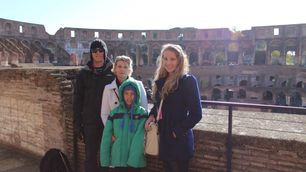 Best friends posing in front of the colosseum on a sunny day; two adults and two children, with the ancient arena in the background.