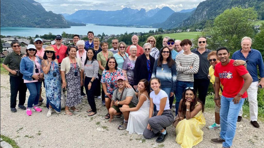 A diverse group of people posing for a photo in front of a scenic lake surrounded by imperial Europe's mountains.