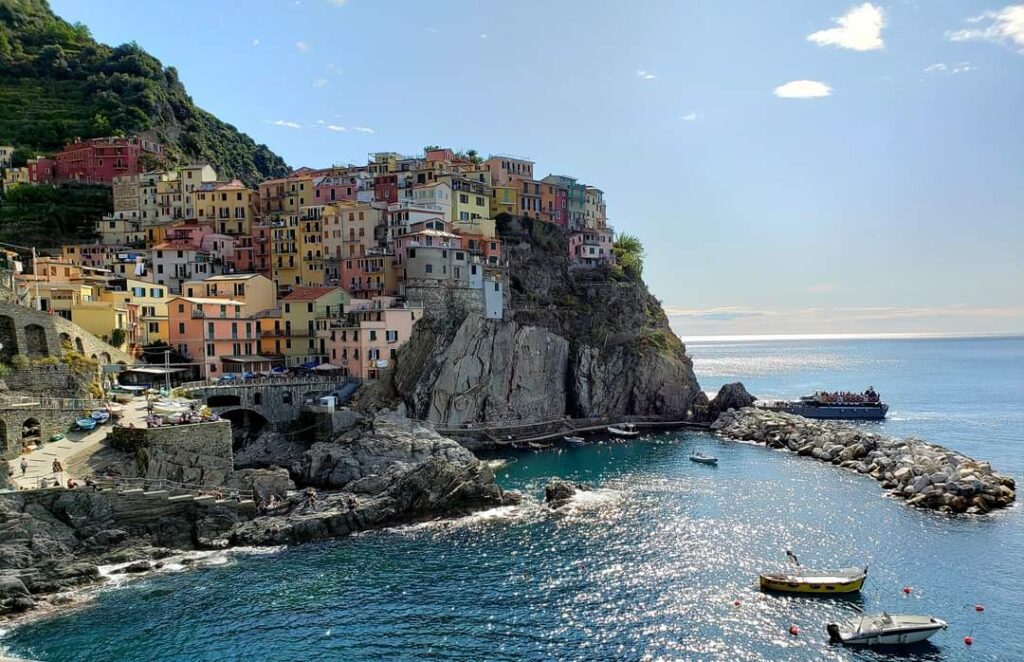 Colorful buildings perched on a rocky cliff overlooking a small harbor with boats, under a clear sky, perfect for solo travelling in Italy.