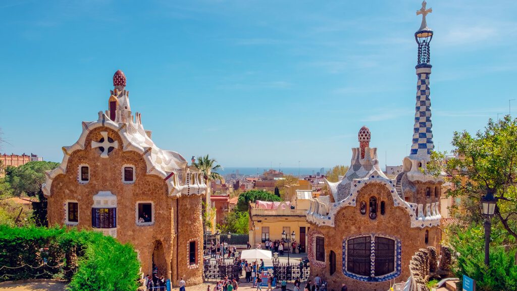 View of Park Güell in Barcelona, a top European summer destination, with whimsical, mosaic-adorned buildings and a clear blue sky.
