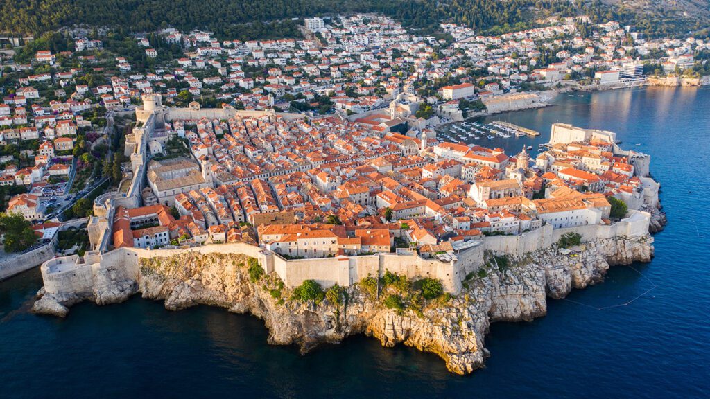 Aerial view of Dubrovnik, Croatia, showcasing the historic walled city surrounded by the Adriatic Sea with modern buildings in the background, a prime example of where to travel in Europe in the