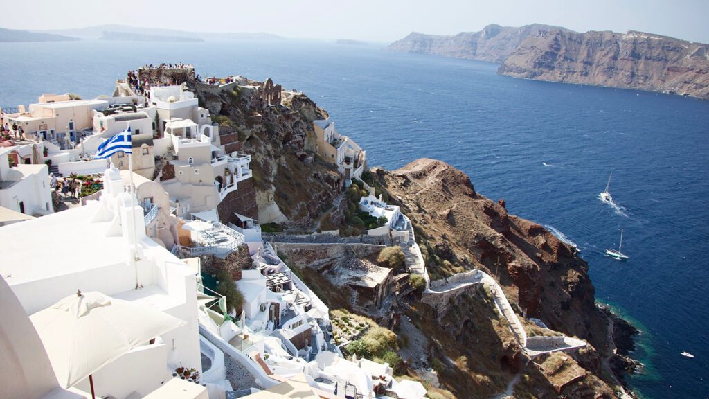Aerial view of Santorini, Greece, showcasing cliffside white buildings with blue accents overlooking the Aegean Sea, one of the best places to visit in Europe during the summer.