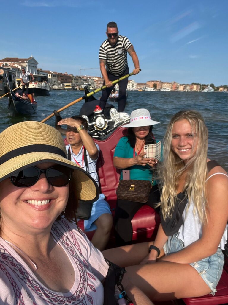 Four tourists enjoying a Mother's Day gondola ride in Venice with a gondolier steering in the background.