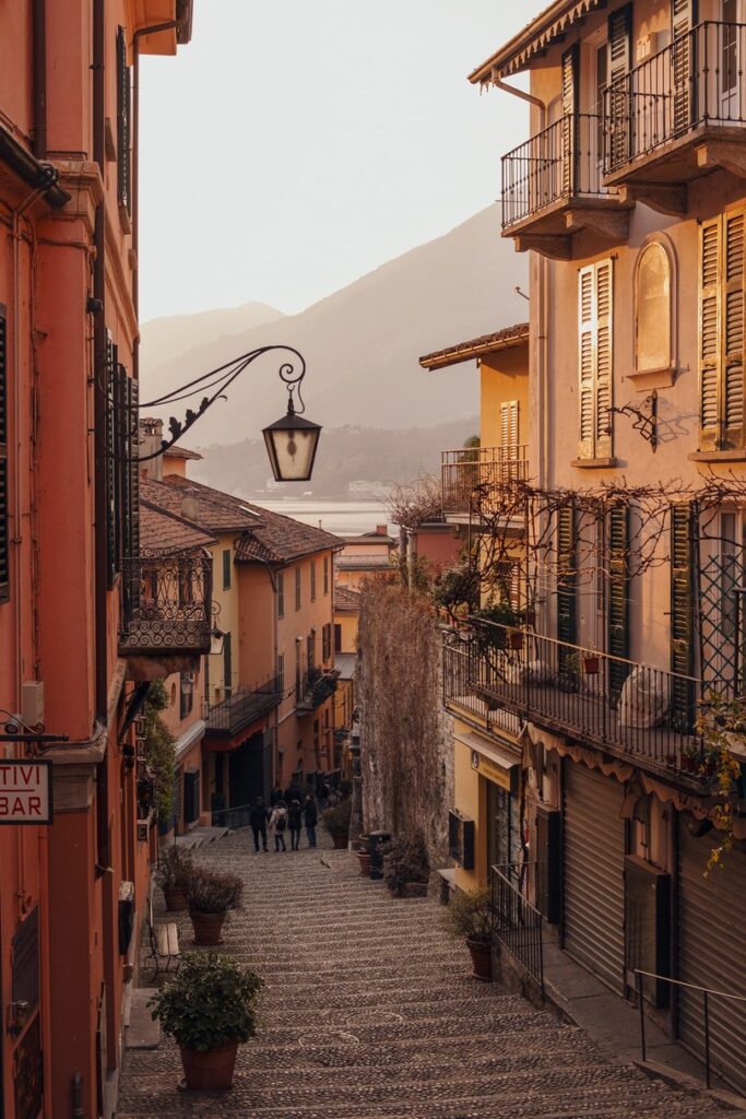 Narrow cobblestone street lined with traditional orange and yellow buildings at sunset, leading to distant mountains in Italy.