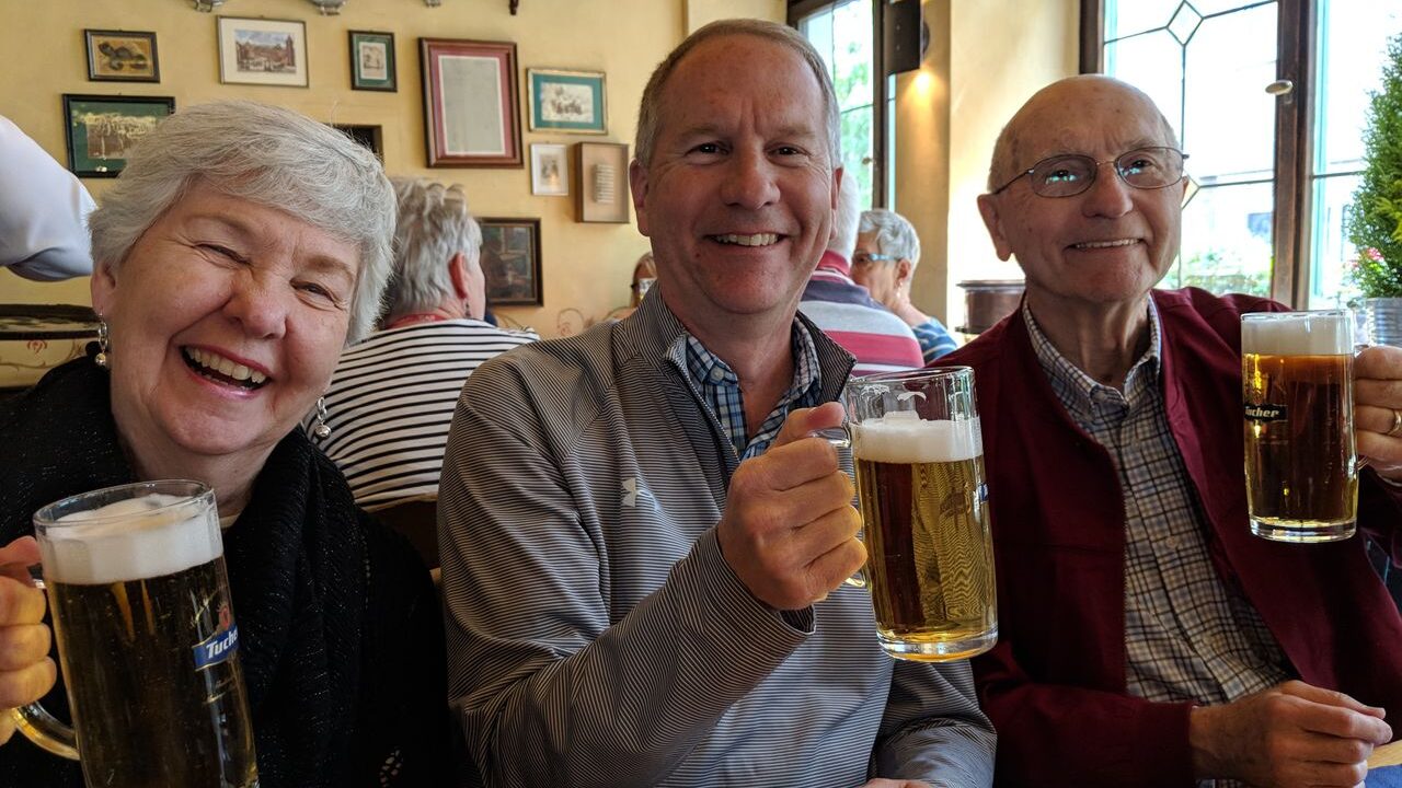 Three people in a bar in Germany posing with beer steins in hand
