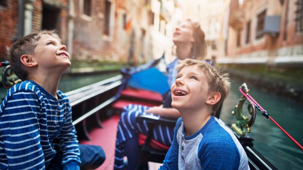 Three young children gawking in awe while enjoying a gondola cruise through Venice, Italy.