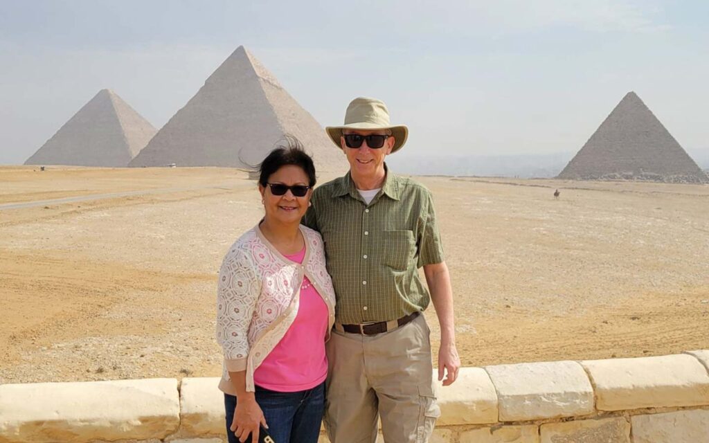 A couple posing in front of the great pyramids of Giza on a sunny day during their Egypt travel story.