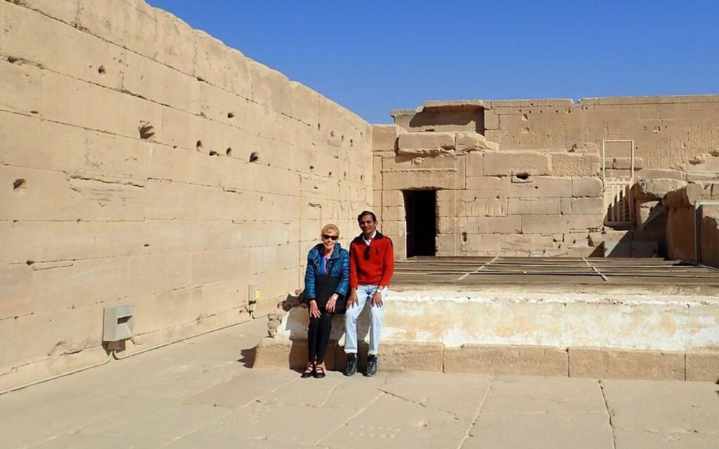 Two people posing together in front of the ancient stone ruins in Egypt under a clear blue sky.