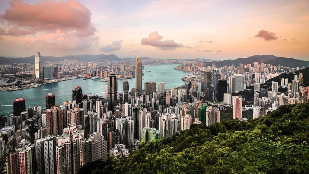 Panoramic view of one of the top 10 most expensive cities in the world, showcasing Hong Kong's skyline and Victoria Harbour from a high vantage point during sunset.