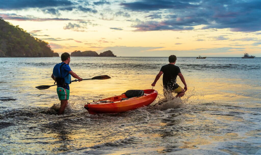 Two men wading out into the sea with a kayak at sunrise