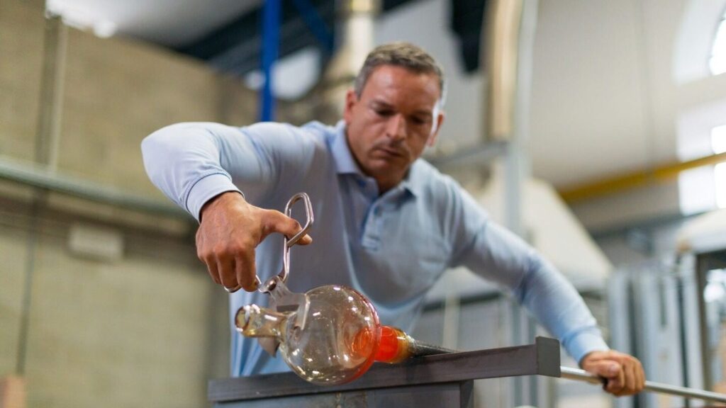 Close up of a glass artisan moulding hot glass on a metal rod