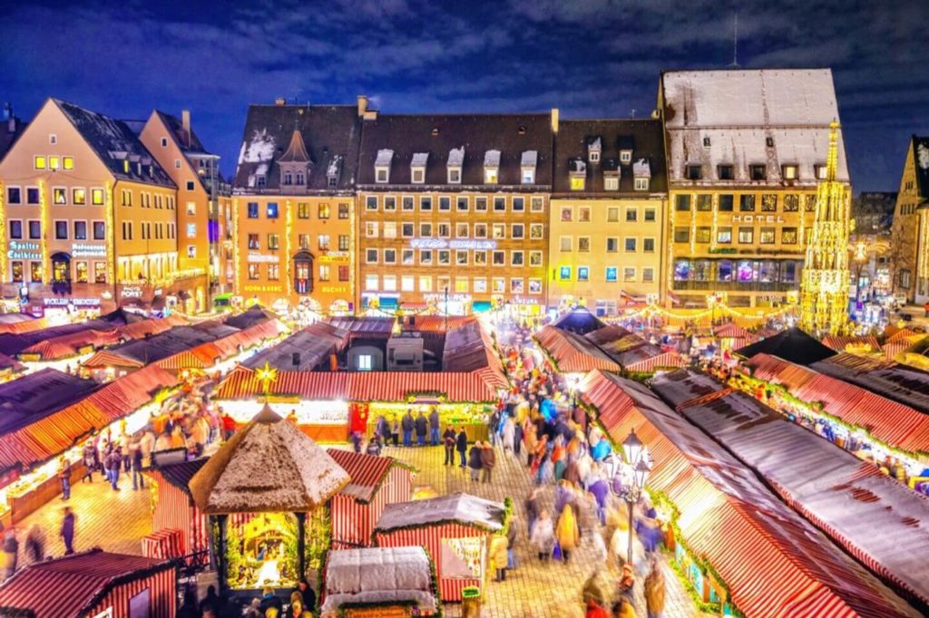 A bustling and vibrant holiday market at nighttime in German winter weather, illuminated by festive lights with a crowd of visitors and traditional market stalls.
