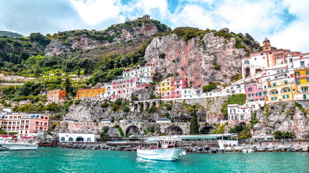 Colorful cliffside town on the Amalfi Coast, buildings lining the side and sea below. Boats in the water.
