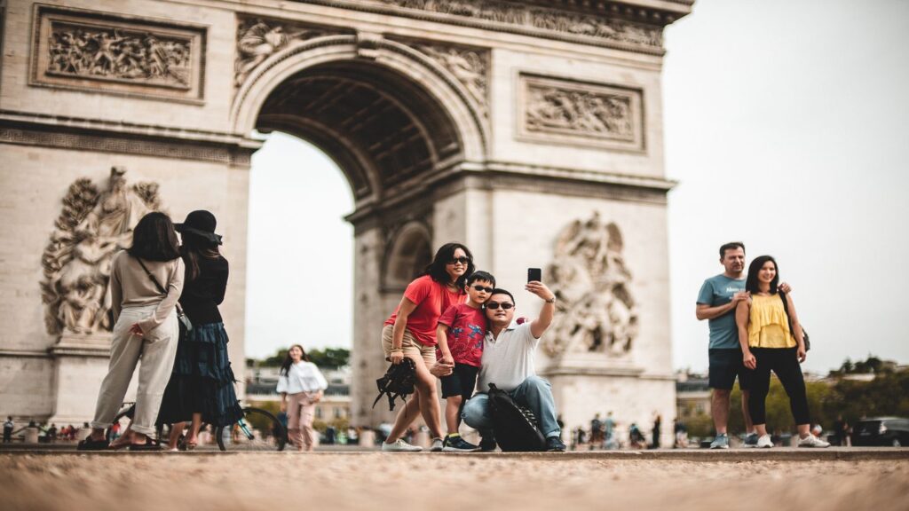 Tourists capturing life-changing travel moments in a selfie in front of the arc de triomphe.