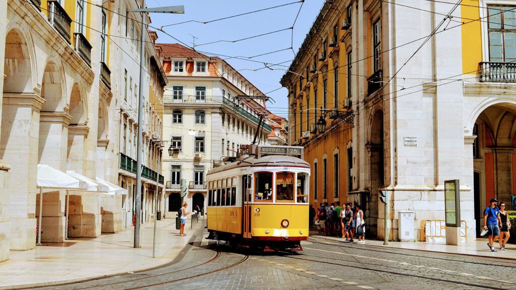 A vintage yellow tram travels through a bustling street lined with classical architecture in a sunny, European city during spring tours.