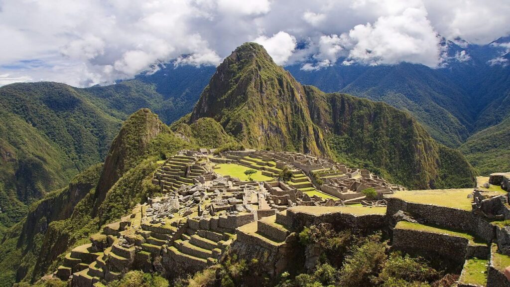 An aerial view of Machu Piccu, framed by the imposing Andes under a cloudy sky.