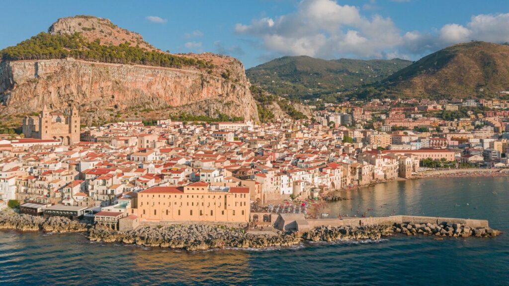 Town in Sicily Italy, many houses all closely lined together. Beach in the distance with umbrellas, people in the sea swimming.