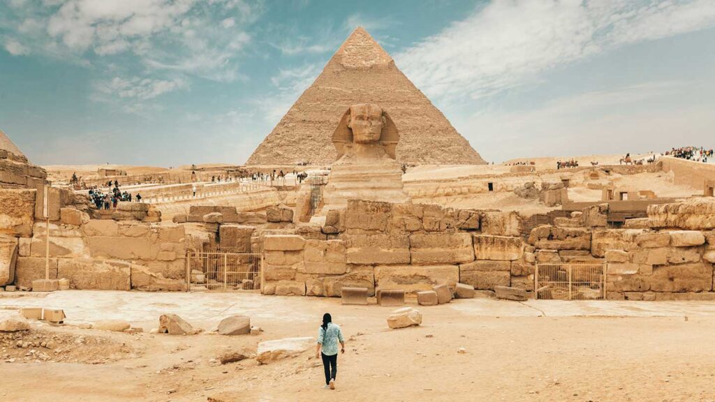 A person embarking on a solo travel adventure towards the great sphinx with the pyramid of Khafre in the background at the Giza Plateau, Egypt.
