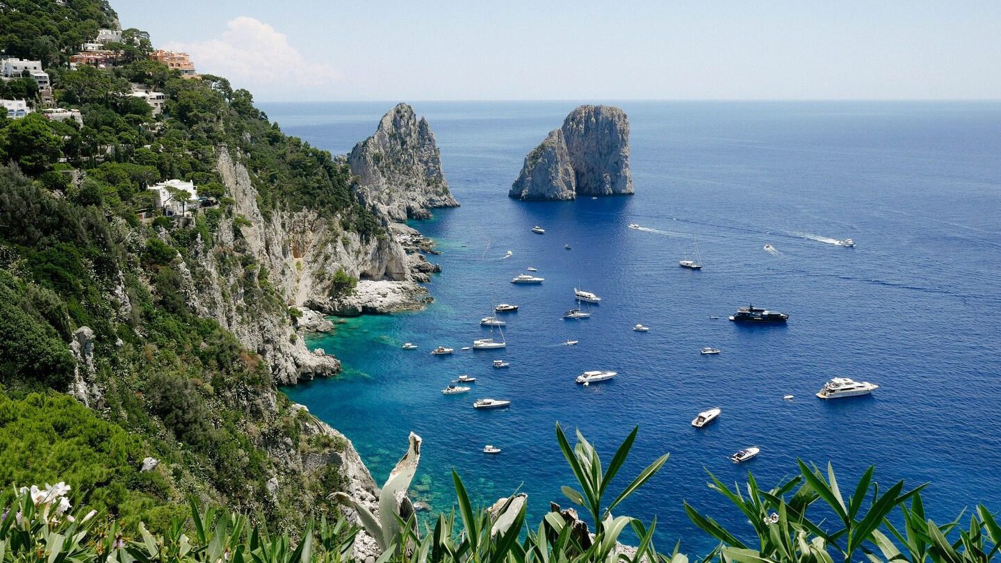 Yachts off the cliff on the Italian coast. Clear blue waters and skies.